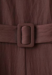 Bruin stof met een brede riem met een rechthoekige gesp. De textuur lijkt glad met subtiele verticale lijnen over het oppervlak.