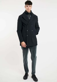 Zwarte dubbelzijdige jas met grote revers, voorzien van een ritssluiting binnenin. Draag over grijs gestreepte broek en zwarte sneakers.