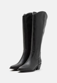 Bottes noires en cuir jusqu'au genou avec un bout pointu, un bord supérieur festonné et un petit talon carré. Texture lisse avec des détails de couture minimaux.