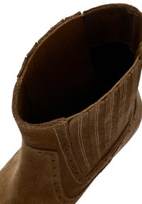 Brown suede ankle boot featuring elastic side panels, vertical stitching, and perforated accents along the sides with a textured interior.