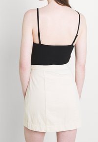 Černý top bez rukávů s tenkými ramínky, zkombinovaný s krémovou mini sukní s hladkým povrchem a skrytým zipem.
