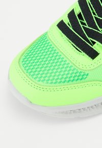 Scarpa sportiva verde neon con tomaia in mesh testurizzato, lacci neri e una suola in gomma traslucida. Presenta dettagli di cucitura a contrasto.