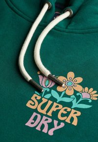 Groene hoodie met witte trekkoorden, met een bloemenontwerp in roze, geel en blauw. "SUPER DRY" in vetgedrukte, multicolore letters gedrukt.