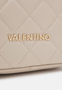 Beige quilted leather handbag with gold "VALENTINO" logo. Features diagonal stitching for texture and a smooth finish.