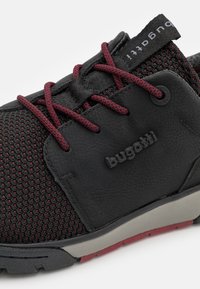 Černé síťované a kožené sneakers s červenými tkaničkami, s texturovaným svrškem, logem a kontrastní šedou a červenou podrážkou.