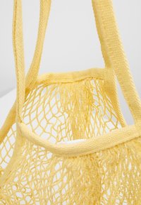 Gele nettas gemaakt van zacht materiaal met dikke, gestructureerde banden. Het open geweven ontwerp maakt de inhoud zichtbaar.