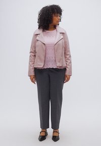 Hellrosa Leder-Bikerjacke über einem rosafarbenen Spitzenstricktop, graue maßgeschneiderte Hosen und schwarze Ballerinas mit Riemchenakzenten.