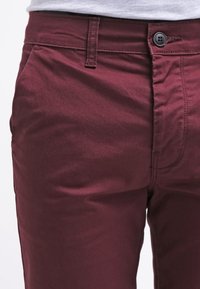 Burgundské bavlněné kalhoty s hladkou texturou, s knoflíkovým zapínáním, předními kapsami a přiléhavým střihem.