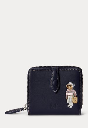 Πορτοφόλι από δέρμα σε ναυτικό μπλε χρώμα, με μπεζ ραφές, λουράκι με κουμπί και εικονογράφηση αρκούδας που φοράει γυαλιά ηλίου, ριγέ πουκάμισο και κρατάει τσάντα tote.