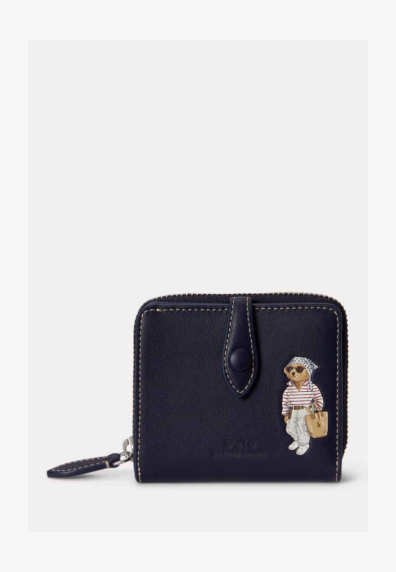 Portefeuille zippé en cuir bleu marine avec coutures beige, sangle à bouton et illustration d'un ours portant des lunettes de soleil, une chemise à rayures et un sac fourre-tout.