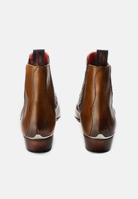 Brown leather ankle boots with a smooth texture, rounded toe, and low stacked heel. Features contrasting black and red pull tabs at the back.