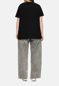 T-shirt noir surdimensionné avec des manches courtes, associé à un pantalon large gris clair. Le T-shirt présente un col rond et une texture lisse.