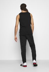 T-shirt preta sem mangas emparelhada com calças de jogging escuras com acentos cinzentos, usada com sapatilhas atléticas brancas e pretas vista por trás.