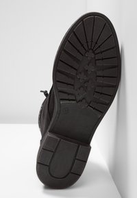 Botín de ante negro con una suela de goma texturizada, que presenta un patrón estriado para mayor agarre y un diseño de punta redondeada, marcado como talla 37.