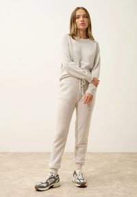 Ljust grått stickat tröja och matchande joggers med dragsko i midjan. Stylad med gråa och vita sportskor. Slät, mjuk textur.