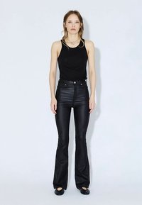 Černý top bez rukávů spárovaný s černými kalhotami s vysokým pasem a rozšířenými nohavicemi. Hladká textura, úzký střih, zapínání na knoflíky vpředu, doplněno černými plochými botami.