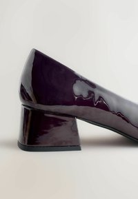 Lilla lakknahast kõrge kontsaga king, millel on kolmnurkne plokknokk, sile tekstuur ja ümar varvas.