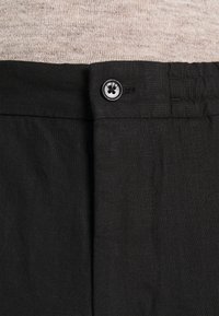 Černé lněné kalhoty s plochým předním dílem, vybavené standardním knoflíkovým zapínáním a jemnou texturou. Jednoduchý design bez viditelných vzorů.