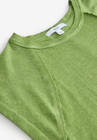 Vihreä puuvillapaita, jossa on pyöreä kaula-aukko, raglan-hihat ja raakamaiset saumat. Kauluksen lähellä oleva etiketti lukee "NEXT". Pehmeä tekstuuri.