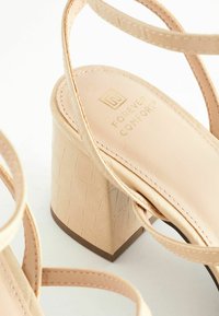 Beige sandály na vysokém podpatku s texturovaným blokovým podpatkem, tenkými páskami a hladkou stélkou s detailem zlatého loga.