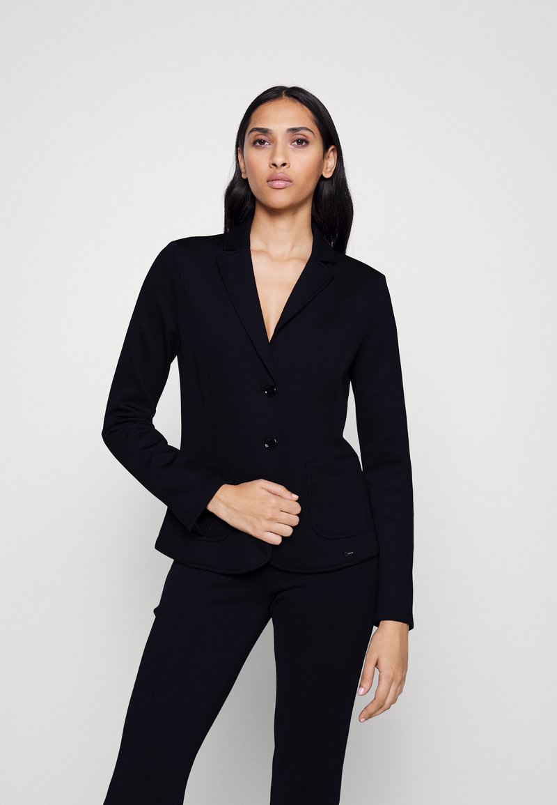 Blazer noir ajusté avec deux boutons, revers cranté et poches à rabat, fabriqué à partir d'un tissu lisse, associé à un pantalon noir assorti.