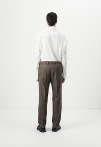 White long-sleeve shirt paired with brown plaid trousers. The outfit features a tailored fit and is complemented by black shoes.