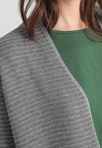 Cardigan gris côtelé avec une texture douce, design à devant ouvert, et un top vert en dessous. Mettez l'accent sur le motif en tricot et l'apparence superposée.