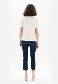 T-shirt bianco a maniche corte, abbinato a jeans neri a vita alta. Il modello indossa sandali grigi chiari. Design semplice, senza motivi visibili.