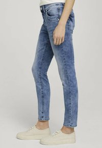 Ljusblå denimjeans med slim fit, fem fickor och subtila blekdetaljer, tillsammans med vita kanvasSneakers.