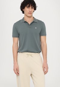 Grijze polo met witte gestreepte kraag, korte mouwen en geborduurd logo, gecombineerd met lichtbeige broek met trekkoord.