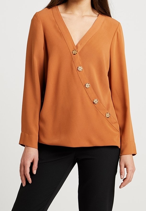 Blusa arancione ruggine con scollatura a V profonda, maniche lunghe e dettaglio dei bottoni diagonale con sei bottoni metallici. Finitura del tessuto liscia.