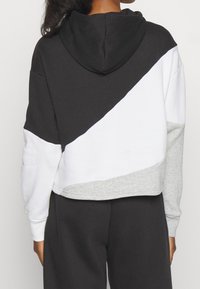 Kraftig hoodie med svart, vit och grå färgblock. Huva som är fäst, mjukt tyg, med en diagonal design över ryggen.