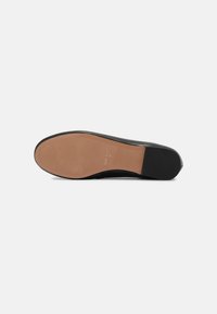 Suela de zapato de cuero negro con un acabado suave en color marrón claro. Tiene una forma redondeada y acentos mínimos. Tacón plano y ligeramente afilado.