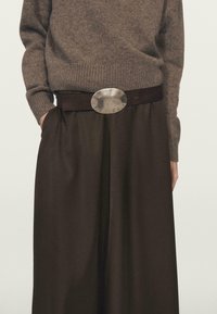 Pull en laine marron à coupe décontractée avec poignets côtelés, associé à un pantalon taille haute marron foncé et une boucle de ceinture ovale métallique.