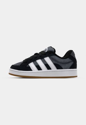 Chaussure de sport noir et gris avec trois rayures blanches, en matériaux daim et mesh, semelle en caoutchouc, et un branding discret sur la languette et le talon.