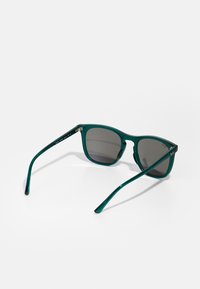 Ochelari de soare din plastic verde cu o ramă rectangulară, lentile întunecate și brațe elegante. Prezintă accente cu logo pe tâmple.