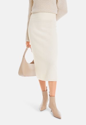 Strickcreme Midi-Rock mit geripptem Bund, kombiniert mit einer beigen Hobo-Tasche und spitzen Ankle-Boots, die eine schlanke, gestreckte Silhouette zeigen.