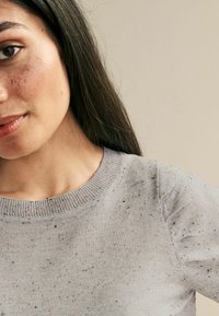 Jasnoszary sweter z okrągłym dekoltem, w różnokolorową, melanżową fakturę, krótki rękaw i ściągacze, prezentujący miękkie wykończenie dzianiny.