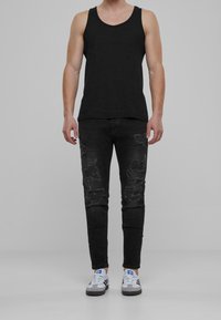 Czarny top na ramiączkach, zniszczone czarne dżinsy z dziurami oraz szare sneakersy z niebieskimi akcentami. Prosty design o dopasowanym kroju.