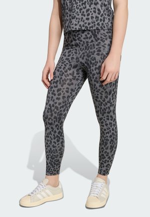 Personne portant des leggings imprimés léopard gris et noir et un haut assorti, associés à des baskets blanches Adidas.