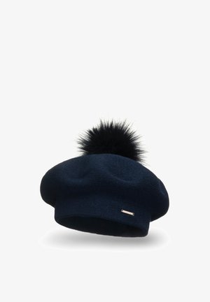 Béret en tricot marine avec un pompon noir sur le dessus. Présente une texture lisse et une petite étiquette métallique sur le côté.