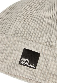Berretto lavorato a maglia in beige chiaro con motivo testurizzato. Presenta una patch quadrata nera con la scritta "Jack Wolfskin" in bianco.