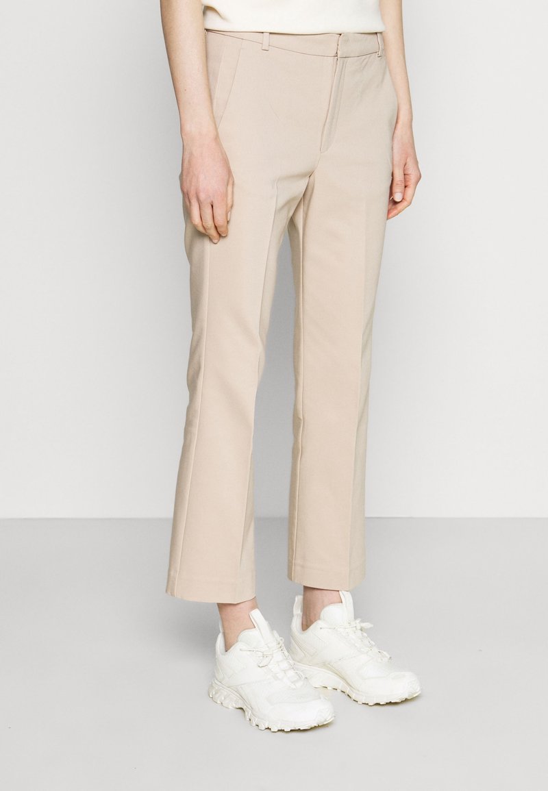 Beige skräddarsydda byxor med slim fit, medelhög midja, slät textur och kort längd, tillsammans med vita sneakers.