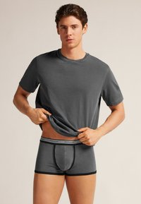 Szary bawełniany t-shirt w zestawie z dopasowanymi szarymi bokserkami, z czarnym elastycznym pasem z logo, prezentując gładki materiał i dopasowany krój.