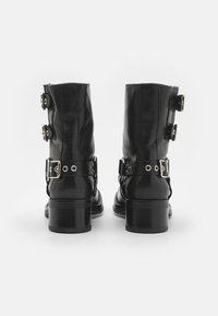 Botas de cuero negro hasta el tobillo con una textura suave, con tres hebillas decorativas y un tacón cuadrado. Vista trasera, diseño minimalista.