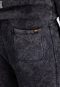 Gros plan sur une poche de pantalon texturée gris foncé avec un petit onglet logo noir et jaune sur la couture.
