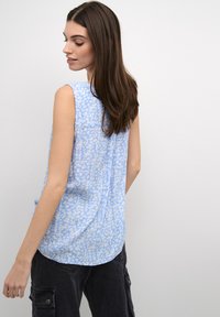 Blusa sin mangas azul con un ligero patrón floral, textura suave y dobladillo curvado. Detalle de costura visible en la parte posterior.