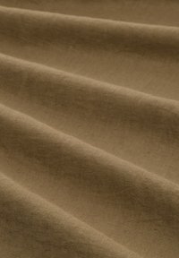 Bežová texturovaná tkanina s jemným, hladkým povrchem má výrazné záhyby a vlny, což naznačuje její měkkou a flexibilní povahu.
