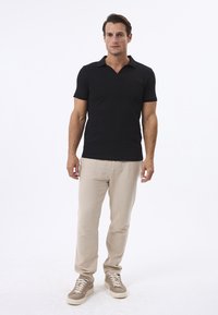 Polo noir à manches courtes avec un motif texturé, associé à un pantalon beige clair et des baskets beiges avec des lacets blancs.
