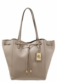 Beżowa skórzana torba tote z złotymi elementami, ściąganym zapięciem i wiszącą metką z logo. Gładka tekstura i otwarta konstrukcja.